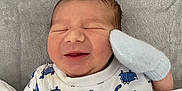 Harry joined the competition — help win amazing prizes! baby, newborn, smiling, blanket, mittens, onesie, blue, white, dinosaur_print, soft_texture, sleeping, infant, cute, cozy, lying_down, indoors, child, face, peaceful, wrapped