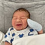 baby, newborn, smiling, blanket, mittens, onesie, blue, white, dinosaur_print, soft_texture, sleeping, infant, cute, cozy, lying_down, indoors, child, face, peaceful, wrapped