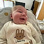 Harry is registered to the contest to win money with this photo: baby, smiling, infant, clothing, bed, bunny, text, indoor, child, cute, sleepwear, person, happy, soft, blanket, white, cozy, portrait, newborn, room