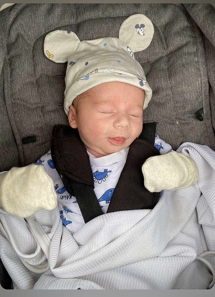 Harry is registered to the contest to win money with this photo: baby, newborn, sleeping, mittens, hat, mickey_mouse, car_seat, blanket, white, gray, infant, cute, child, resting, cozy, clothing, soft, portrait, indoors, peaceful