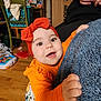 Aela joined the competition — help win amazing prizes! adult_hand, baby, big_eyes, blue_blanket, bow_headband, cardboard_box, colorful_clothing, floral_skirt, green_chair, hand, hardwood_floor, indoor, infant, laundry_basket, living_room, orange_clothing, plush_blanket, portrait, smile, toy