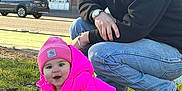 Aela is registered to the contest to win money with this photo: adult_male, affectionate_interaction, baby, black_hoodie, boots, crawling, daylight, grass, jeans, outdoor, parked_car, person, pink_beanie, pink_jacket, sidewalk, smiling, sunglasses, toddler, urban_building, watch