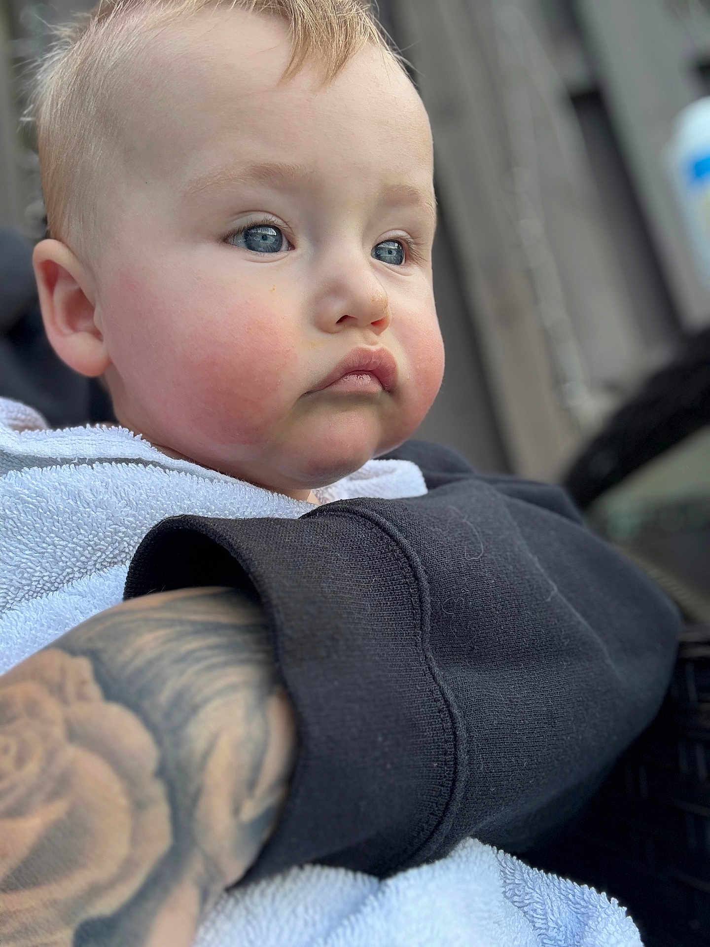 Arlo joined the competition — help win amazing prizes! baby, child, face, blue_eyes, cheeks, towel, tattoo, arm, clothing, black_sleeve, portrait, closeup, skin, expression, person, indoors, soft_light, blurred_background, curly_hair, gaze