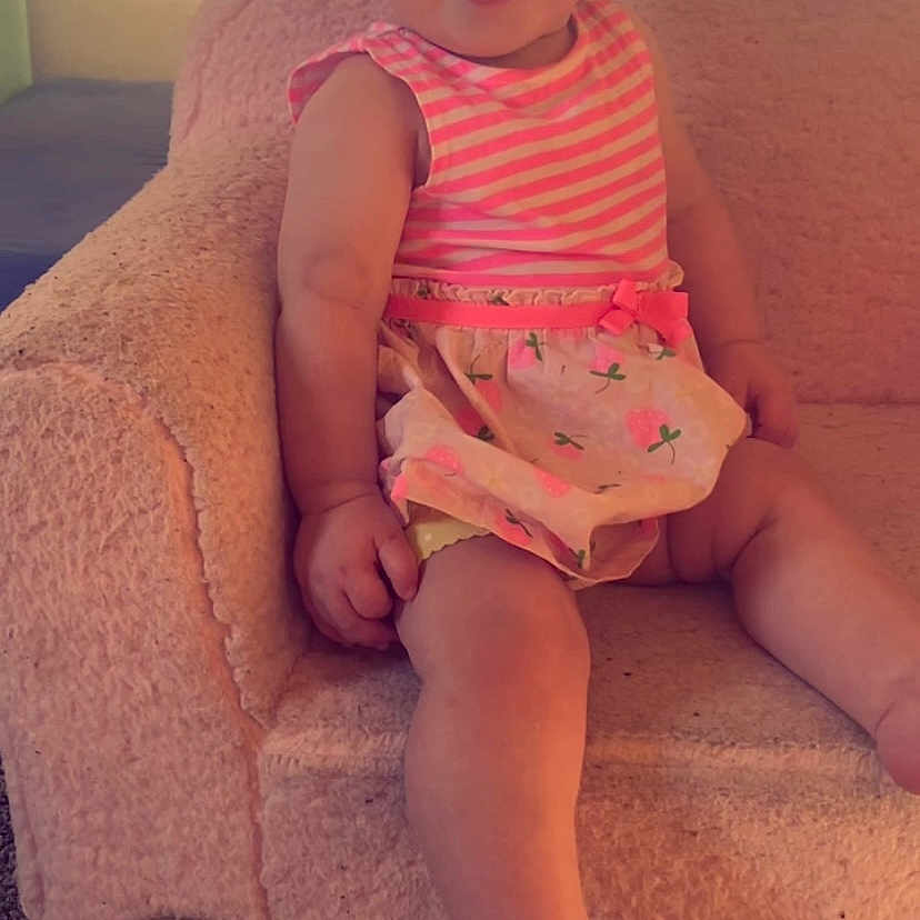 Paige is registered to the contest to win money with this photo: baby, carpet, chair, child, cute, floral_pattern, foot, hand, happy, indoor, infant, one_year_old, pink_dress, portrait, sitting, skin, smiling, soft_furniture, striped_clothing, twelve_months_sign