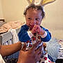 Brandon is registered to the contest to win money with this photo: baby, bunny_ears, smiling, pajamas, child, indoor, bedroom, person, hands, cute, happy, infant, curly_hair, bracelet, furniture, bed, blanket, toy_pattern, playful, holding