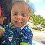 Brandon is registered to the contest to win money with this photo: child, toddler, smiling, tongue_out, blue_clothing, green_trim, car_interior, window, suburban, houses, trees, daylight, happy, cute, portrait, face, earrings, curly_hair, seat, casual
