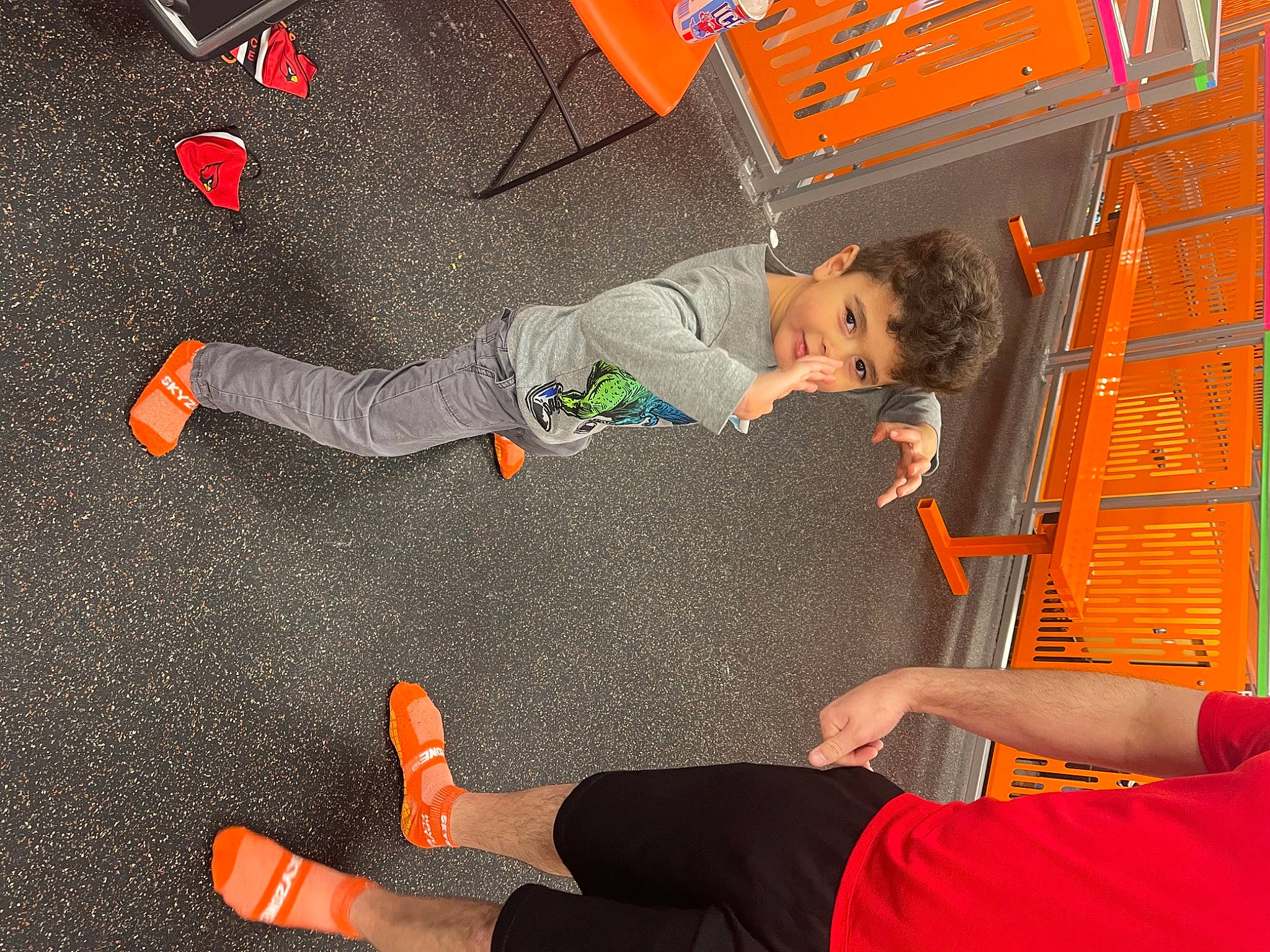 Jaxson is registered to the contest to win money with this photo: child, clothing, floor, flooring, foot, fun, gesture, human_leg, joint, knee, orange, person, play, recreation, red, sneakers, sportswear, t_shirt, thigh, toddler
