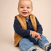 Kaïs a rejoint le concours — aidez-le/la à gagner de superbes lots ! baby, child, smiling, sitting, vest, jeans, shoes, indoor, portrait, happy, cute, young, casual_clothing, studio, playful, hands, face, footwear, light_background, person