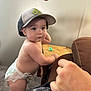 baby, baseballcap, bodypart, cap, clothing, couch, diaper, eating, face, finger, food, furniture, hand, hat, head, person, photography, portrait, shorts, sitting