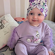 Grace joined the competition — help win amazing prizes! baby, child, face, smile, headwrap, clothing, sitting, bed, blanket, pillow, purple, pattern, indoor, happy, cute, person, toddler, apparel, portrait, home