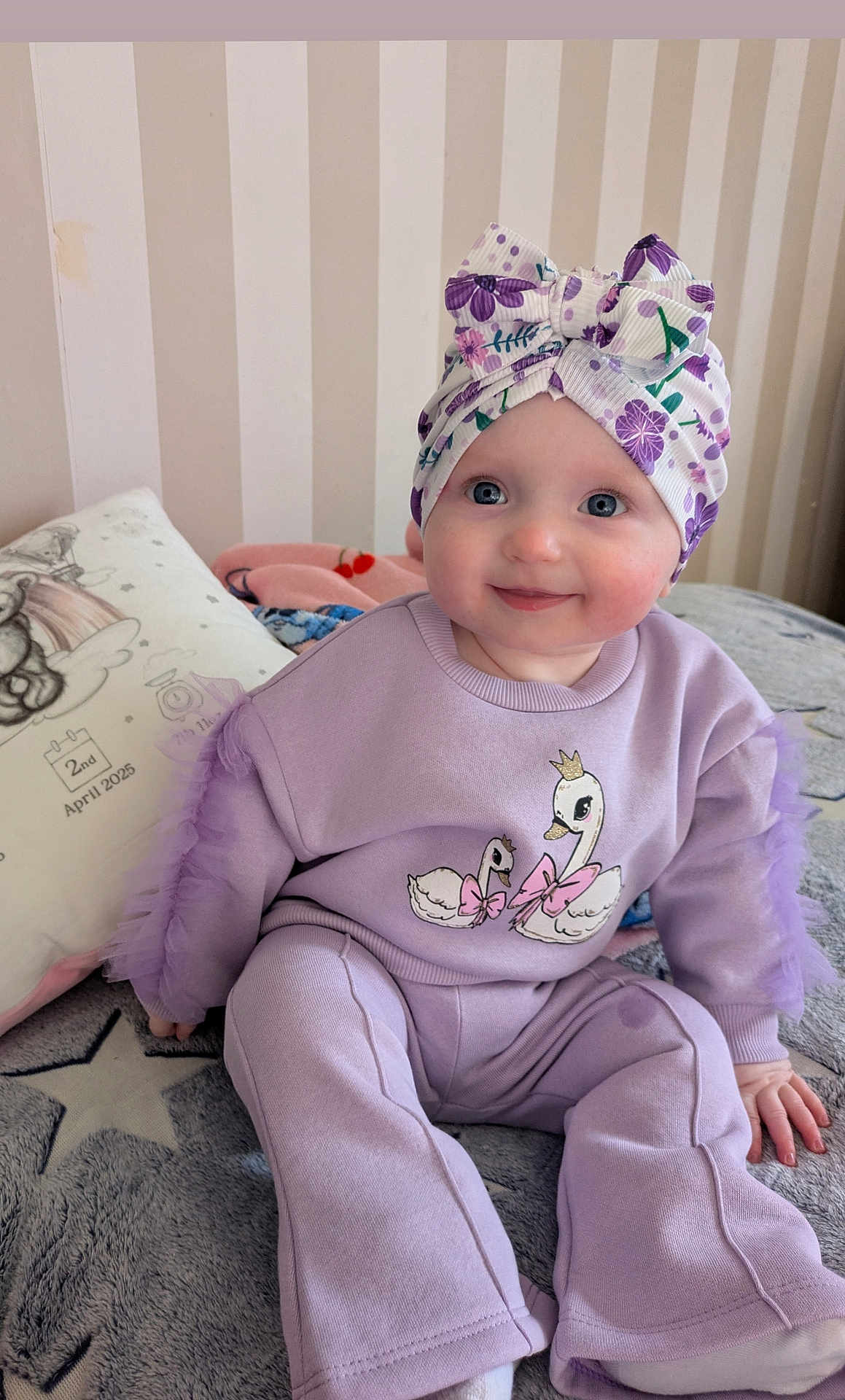 Grace joined the competition — help win amazing prizes! baby, child, face, smile, headwrap, clothing, sitting, bed, blanket, pillow, purple, pattern, indoor, happy, cute, person, toddler, apparel, portrait, home