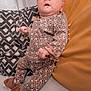 baby, infant, leopard_print, headband, slippers, pillow, blanket, cozy, sparkles, cute, indoors, clothing, child, person, soft_texture, smiling, resting, patterned_clothing, comfortable, young_child