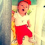 baby, infant, crib, headband, flower, red_pants, white_shirt, sneakers, giraffe_blanket, toy, colorful, sleeping_area, cute, child, lying_down, wide_eyes, open_mouth, soft_toys, mesh_side, comfort