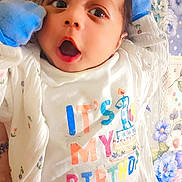 Yousuf joined the competition — help win amazing prizes! baby, infant, mittens, clothing, onesie, birthday, face, expression, lying_down, blanket, floral_pattern, cute, child, person, celebration, happy, closeup, skin, head, mouth_open
