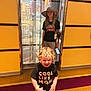 Ace joined the competition — help win amazing prizes! child, toddler, kid, curly_hair, hat, stuffed_toy, smartphone, tshirt, shorts, indoor, elevator, yellow_wall, carpet, smile, standing, happy, playful, person, portrait, casual_clothing