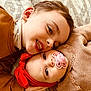 baby, child, sibling, pacifier, headband, smile, face, portrait, lying_down, cozy, warm_colors, clothing, cute, indoor, happy, toddler, family, expression, close_up, blanket