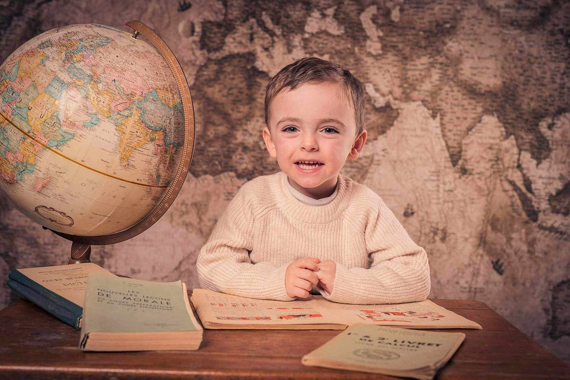 Mattia a rejoint le concours — aidez-le/la à gagner de superbes lots ! child, smiling, desk, books, globe, map, vintage, education, indoors, portrait, young, sweater, reading, study, world, geography, happy, curly_hair, hands, table
