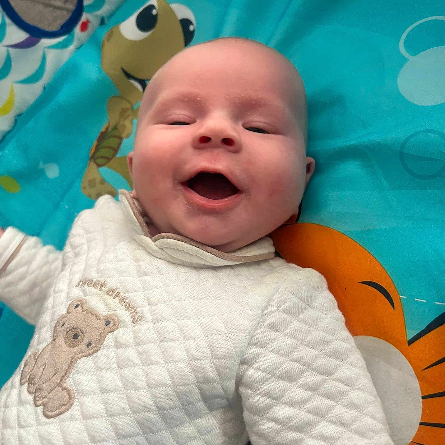 Lillie-Mai is registered to the contest to win money with this photo: baby, bear_embroidery, blue, cartoon, child, colorful, cute, face, happy, indoors, infant, joyful, orange, person, play_mat, portrait, quilted_clothing, smiling, turtle, white