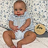 baby, infant, child, sitting, portrait, smiling, bed, bedroom, pillow, blanket, floral, wooden_plaque, milestone, five_months, blue_clothing, bare_feet, face, indoors, home, photography
