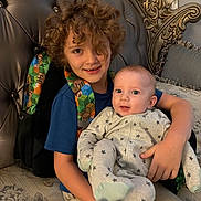 Sebastian joined the competition — help win amazing prizes! child, baby, smiling, curly_hair, backpack, blue_shirt, star_pajamas, couch, decorative_pillow, indoor, portrait, happy, seated, holding, furniture, home, sibling, cute, people, family
