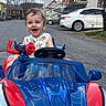 toddler, child, toy_car, spiderman, red, blue, outdoor, street, residential_area, happy, smiling, curly_hair, vehicle, playtime, daylight, car_toy, person, fun, cute, joyful