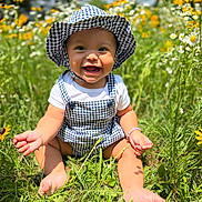 Evelyn joined the competition — help win amazing prizes! baby, child, smiling, hat, checkered, overalls, grass, flowers, sunlight, outdoor, nature, greenery, happy, sitting, cute, summer, toddler, field, playful, sunny