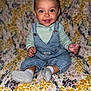 Evelyn joined the competition — help win amazing prizes! baby, blanket, bright, child, clothing, cozy, cute, denim_overalls, face, feet, floral_pattern, gray_socks, hands, happy, indoors, infant, portrait, sitting, smiling, young_child