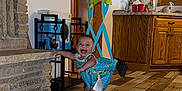Evelyn joined the competition — help win amazing prizes! baby, baby_clothes, baby_jumper, baby_toy, barefoot, child, countertop, door, floor, happy, harness, indoor, kitchen, person, plastic_container, red_cups, smiling, stone_fireplace, window, wooden_cabinets