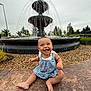 Evelyn joined the competition — help win amazing prizes! baby, bench, child, cute, daytime, dress, fountain, grass, happy, infant, nature, outdoor, park, playful, sitting, sky, smile, stone_path, trees, water