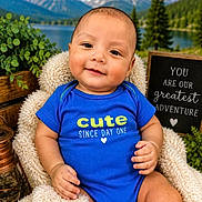 Storm is registered to the contest to win money with this photo: baby, child, infant, smiling, portrait, blue_onesie, cute, seated, chair, fluffy_blanket, lake, mountains, snowy_peaks, forest, outdoor, scenic_background, sign, heart_symbol, photography, happy