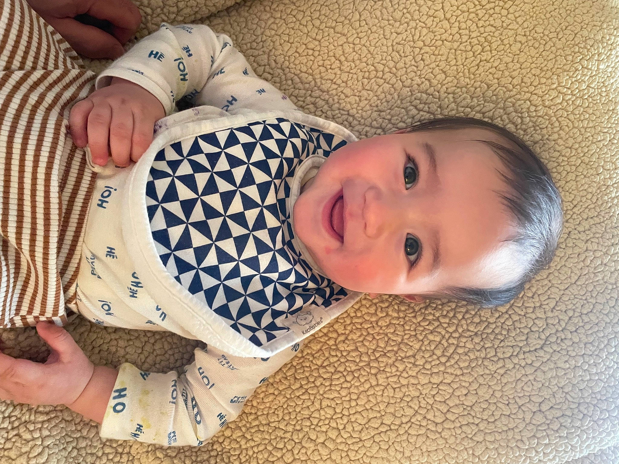 Korben is registered to the contest to win money with this photo: baby, baby_toddler_clothing, cheek, child, comfort, elbow, finger, flooring, hand, happy, human_leg, joy, linens, nail, pattern, person, sleeve, smile, thumb, toddler