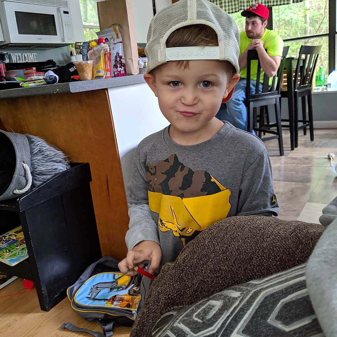 Jaxson is registered to the contest to win money with this photo: cap, child, ear, electronic_device, furniture, hat, head, headgear, headwear, helmet, house, person, play, sitting, smile, square, t_shirt, table, technology, toddler