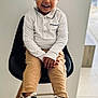 Kendy participe au concours pour gagner de l'argent avec cette photo : child, toddler, smiling, curly_hair, white_shirt, tan_pants, white_sneakers, chair, indoor, floor_tiles, modern_chair, person, happy, sitting, casual_clothing, cute, portrait, young_child, hands, feet