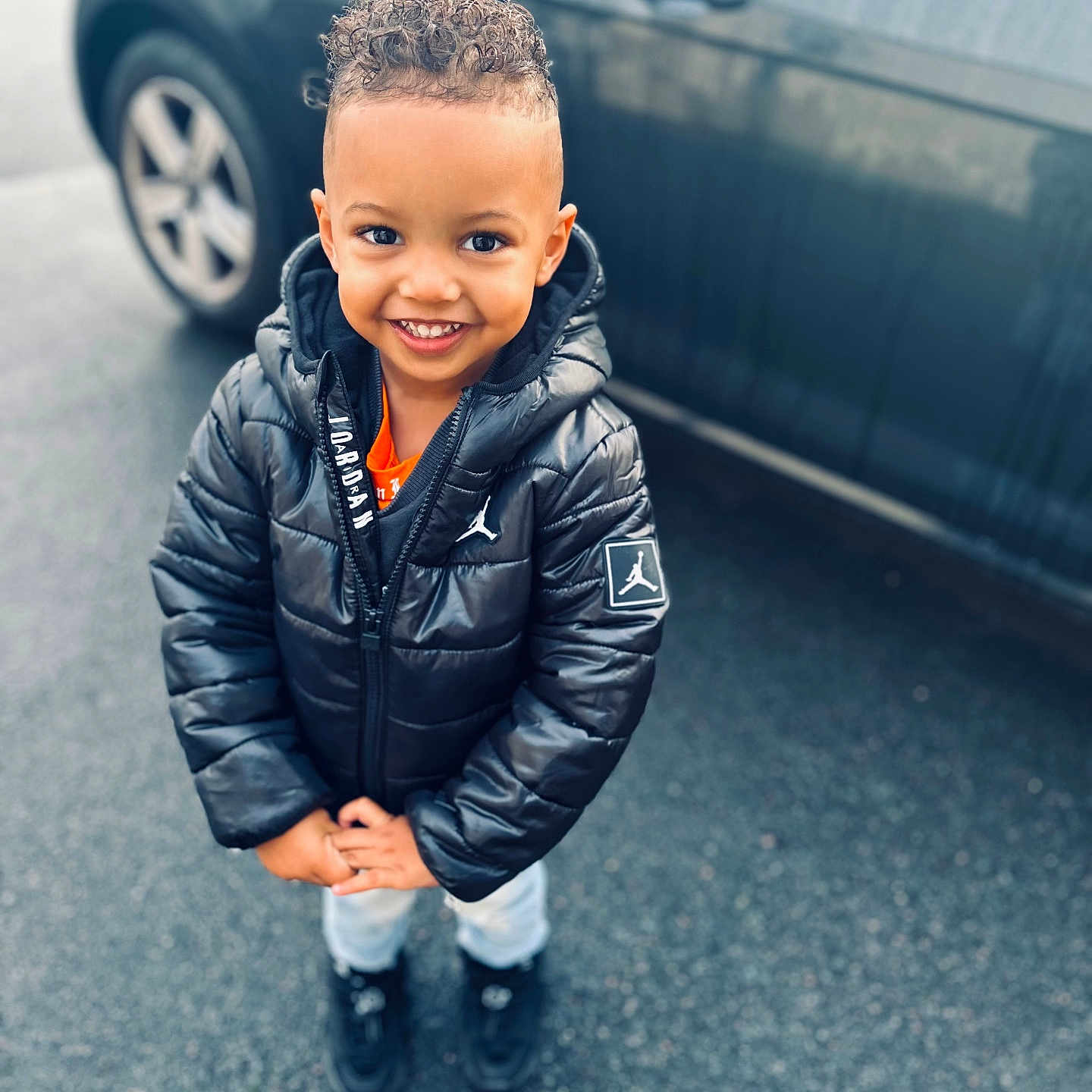 Kendy a rejoint le concours — aidez-le/la à gagner de superbes lots ! asphalt, black_jacket, black_shoes, car, casual, child, curly_hair, cute, daytime, happy, hoodie, jeans, jordan_logo, outdoor, portrait, smiling, standing, urban, winter_clothing, young_child