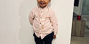 Kendy a rejoint le concours — aidez-le/la à gagner de superbes lots ! toddler, child, smiling, standing, indoor, white_wall, tile_floor, curly_hair, button_up_shirt, gold_chain, dark_pants, white_sneakers, happy, portrait, casual_clothing, young_child, floor_tiles, shadow, home_interior, cute