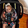 baby, car_seat, child, comfortable, cute, floral_outfit, happy, headband, indoor, infant, person, playful, safety_harness, seat, sitting, smiling, straps, toddler, wooden_floor, young_child