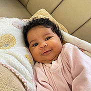 Luna participe au concours pour gagner de l'argent avec cette photo : baby, smiling, curly_hair, pink_clothing, blanket, couch, soft_texture, indoor, portrait, infant, cute, happy, person, face, head, cozy, warm, resting, comfort, young_child