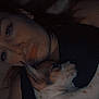person, dog, puppy, lying_down, close_up, sleepy, indoor, bed, blanket, snuggling, dark, face, pet, cozy, resting, cute, animal, companion, human, affection