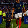 soccer_player, dog, stadium, crowd, flag, sports_uniform, grass, leash, team_captain, sport_event, referee, athlete, celebration, competition, national_team, blue_jersey, red_socks, number_10, walking, outdoor