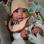 Rmani joined the competition — help win amazing prizes! baby, infant, hat, bib, blanket, hand, face, eyes, clothing, pattern, colorful, geometric_pattern, indoor, seated, cute, portrait, child, young, soft_texture, warm