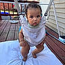 baby, child, curly_hair, baby_jumper, outdoor, wooden_deck, pillow, curious, infant, sitting, playtime, cute, face, person, daylight, home, fence, expression, clothing, safety