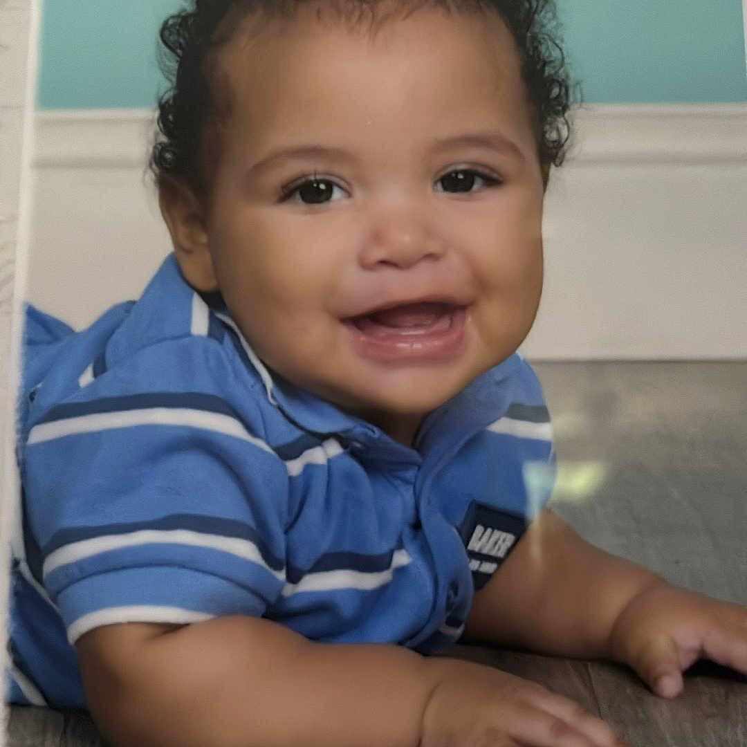 Rmani joined the competition — help win amazing prizes! baby, smiling, blue_shirt, striped_clothing, curly_hair, lying_down, floor, child, portrait, happy, infant, cute, indoors, person, head, face, young, six_months, skin, expression