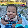 Rmani joined the competition — help win amazing prizes! baby, child, walker, toy, outdoor, smiling, curly_hair, bib, happy, grass, backyard, sunlight, person, play, closeup, infant, face, blue, clothing, seat