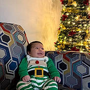 Rafael is registered to the contest to win money with this photo: baby, celebration, child, christmas_tree, couch, cozy, decorations, festive, green_outfit, happy, holiday, home, indoor, infant, lights, patterned_fabric, portrait, red_socks, seated, smiling