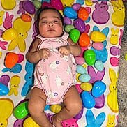 Imani joined the competition — help win amazing prizes! baby, infant, onesie, pink_clothing, bunny_pattern, colorful_blanket, easter_eggs, plastic_eggs, lying_down, indoors, cute, chubby_legs, face, hands, feet, playful, holiday_theme, festive, child, portrait