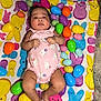 baby, infant, onesie, pink_clothing, bunny_pattern, colorful_blanket, easter_eggs, plastic_eggs, lying_down, indoors, cute, chubby_legs, face, hands, feet, playful, holiday_theme, festive, child, portrait