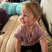 Xalia is registered to the contest to win money with this photo: toddler, child, smile, braid, bed, blanket, plush_toy, indoor, happy, clothing, person, portrait, furniture, soft_toys, casual, cute, young_child, sitting, pink_shirt, black_pants