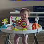 baby, child, activity_walker, toy, indoor, floor, pink_onesie, books, television, smiling, happy, person, furniture, carpet, legs, face, hair, play, home, living_room
