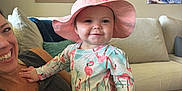 Annie is registered to the contest to win money with this photo: baby, child, woman, smile, hat, flamingo, clothing, couch, indoor, painting, wall_art, living_room, person, happy, portrait, casual, furniture, home, relaxation, sun_hat