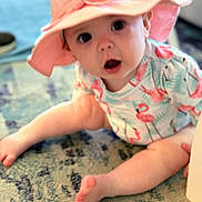 Annie joined the competition — help win amazing prizes! baby, child, hat, pink, flamingo, pattern, sitting, rug, indoor, curious, wide_eyes, open_mouth, infant, cute, legs, foot, clothing, person, headwear, expression